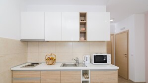 A compact kitchen with white cabinets, a microwave, a sink, and a small fruit basket. - Apartments Marmo (Zupa dubrovacka)