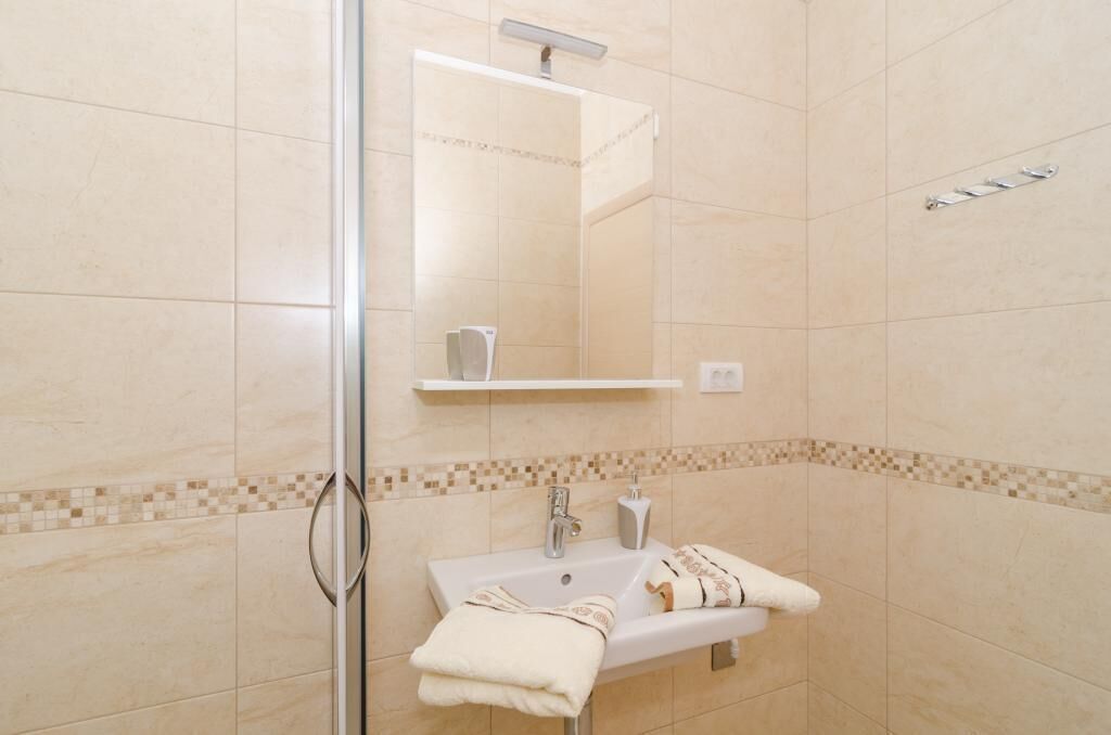 A bathroom with a glass shower enclosure, a sink with a mirror above it, and a towel rack.