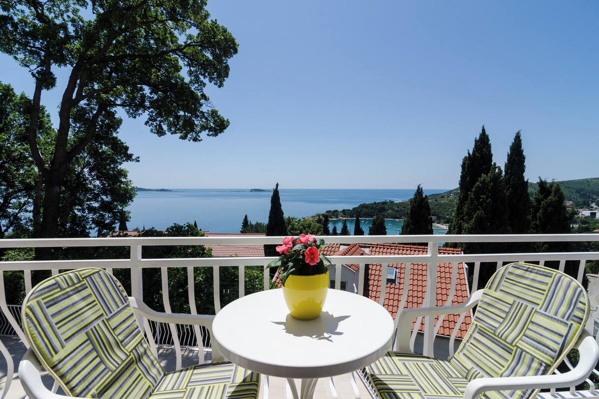 A balcony with two striped chairs and a small table with a yellow vase and pink flowers.