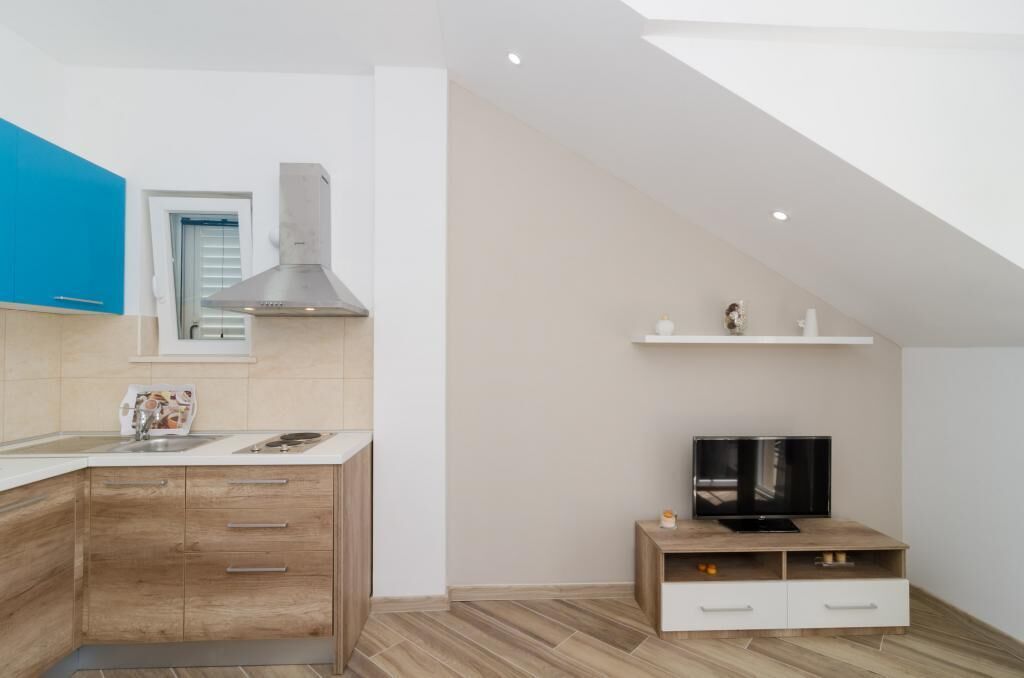 Una cocina moderna con armarios de madera, estufa integrada y un televisor sobre un pedestal de madera.