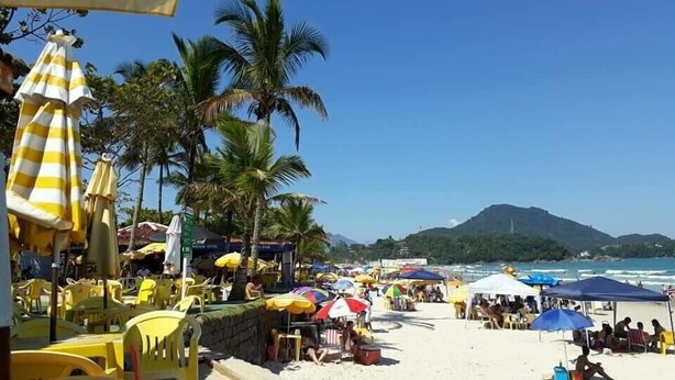 Una spiaggia con ombrelloni gialli e bianchi a righe, palme e una montagna sullo sfondo.