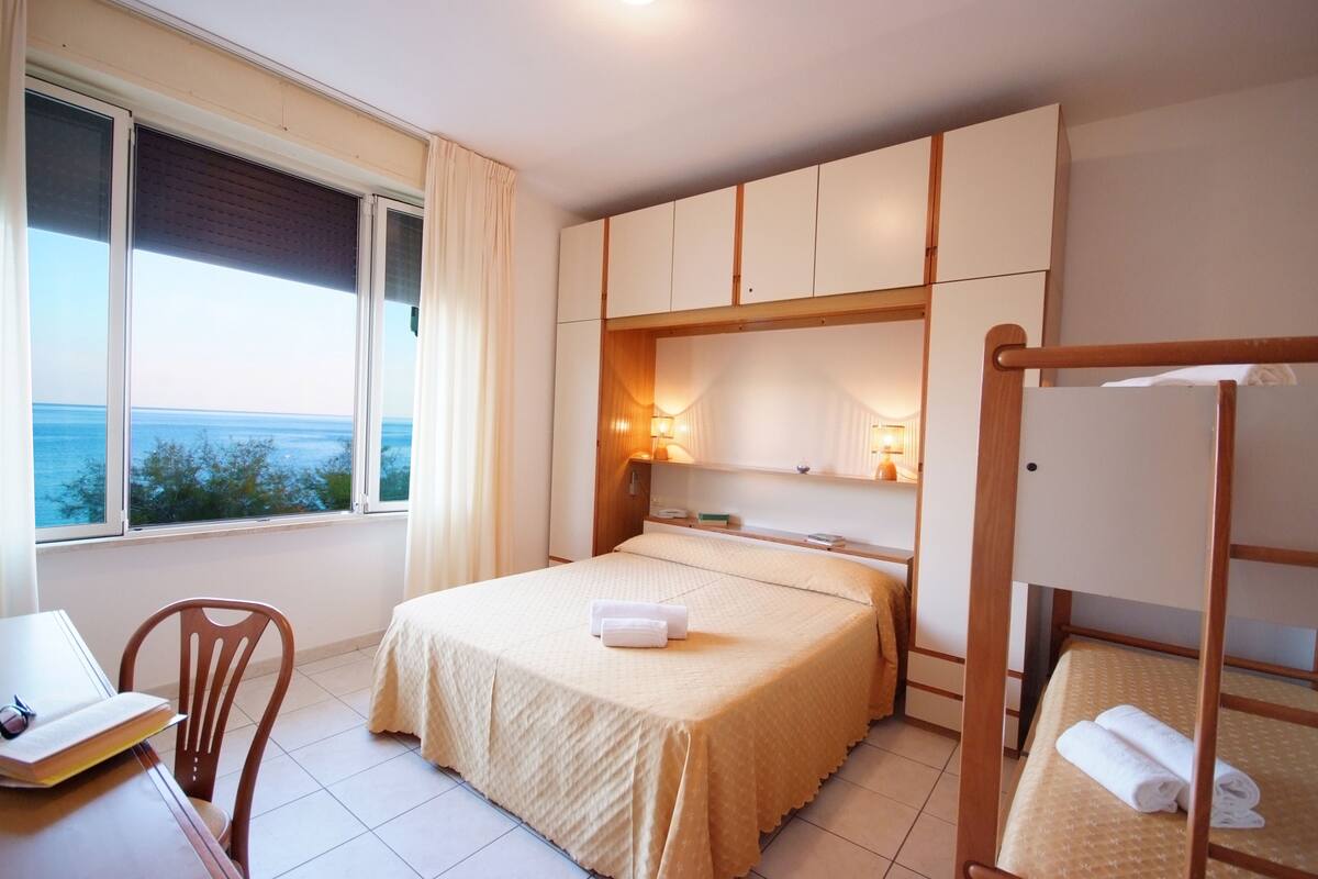 Ein Hotelzimmer mit einem Bett, einem Schreibtisch mit Stuhl, einem Etagenbett und Blick auf das Meer.