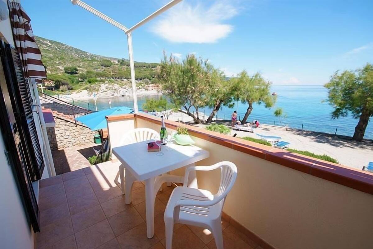 Ein Balkon mit Tisch und Stühlen, mit Blick auf einen Strand und einen Poolbereich.