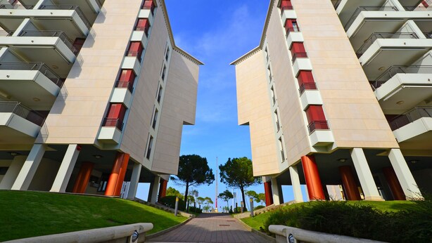 Un edificio simétrico con varios balcones y un camino central que lleva a un asta de bandera.