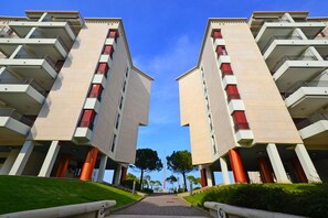 A symmetrical building with multiple balconies and a central pathway leading to a flagpole. - Condominio Porta del Mare (Lignano Sabbiadoro)