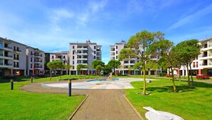 Un moderno complejo residencial con varios edificios de apartamentos, un área pavimentada central y zonas verdes circundantes.