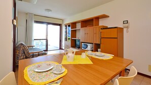 Comedor con mesa de madera dispuesta para dos personas, microondas y refrigerador al fondo.