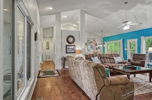 A spacious living room with a large sectional sofa, a ceiling fan, and a view of the outdoors through large windows.