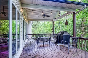 A covered deck with outdoor furniture, a grill, and string lights.