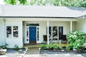 A single-story house with a blue front door, two windows, and a porch with two chairs.