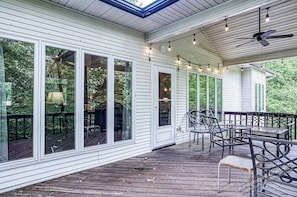 A covered deck with large windows, outdoor furniture, and string lights.