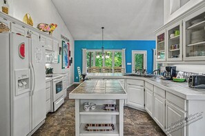 A kitchen with white cabinets, a central island, a refrigerator, and a dining area with chairs and a table.