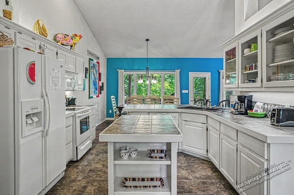 A kitchen with white cabinets, a central island, a refrigerator, and a dining area with chairs and a table.