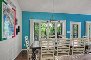 A dining area with a large table, multiple chairs, a chandelier, and a window with curtains.