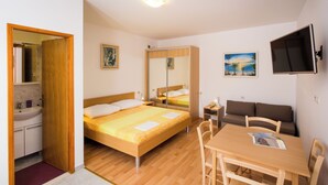 A bedroom with a wooden bed, a bedside table, a mirror, a TV, a sofa, and a dining area with chairs. - Apartments Bibijana (Zupa dubrovacka)