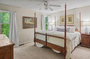 Un lit à baldaquin avec un ventilateur de plafond, une table de chevet avec une lampe et deux tableaux encadrés accrochés au mur.