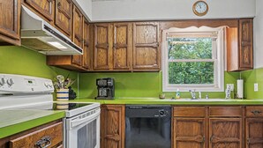 A kitchen with wooden cabinets, a dishwasher, a stove, and a window with a view of trees.