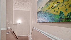 A staircase with a handrail, a light fixture, and a painting of a landscape on the wall.