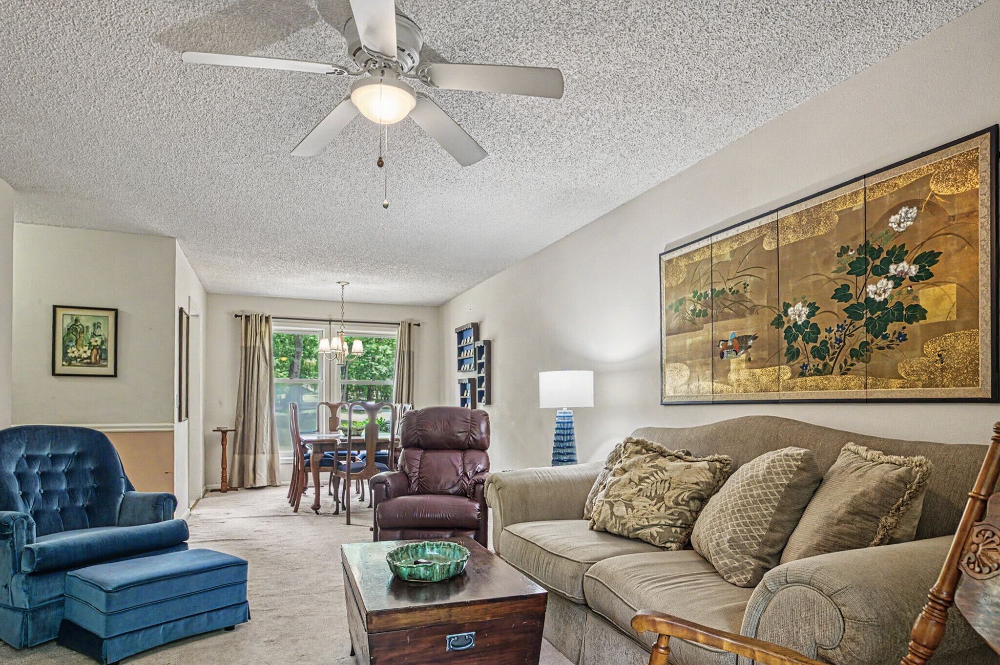 A living room with a ceiling fan, a blue armchair, a brown leather chair, a beige sofa, and a wooden coffee table.
