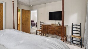 A bedroom with a four-poster bed, a wooden dresser, a television, and a chair.