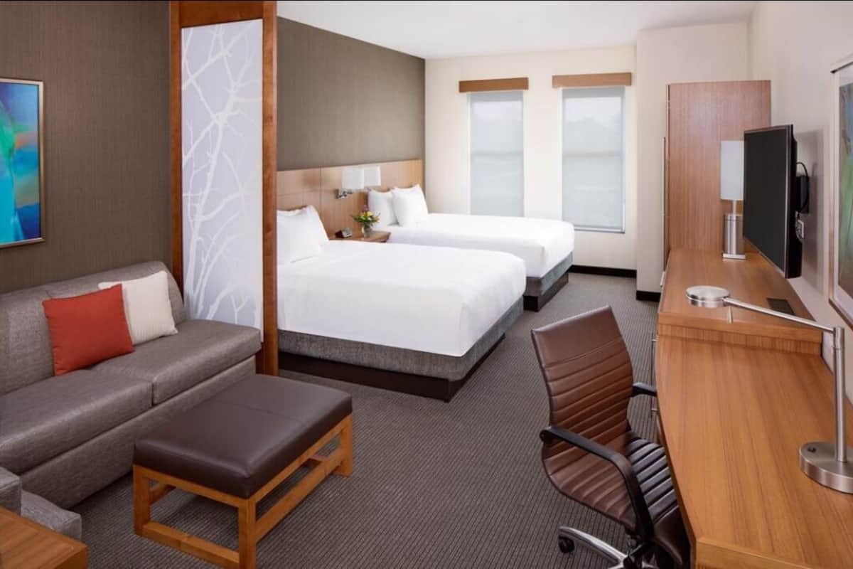 A hotel room with two beds, a sofa, a desk with a TV, and a window.