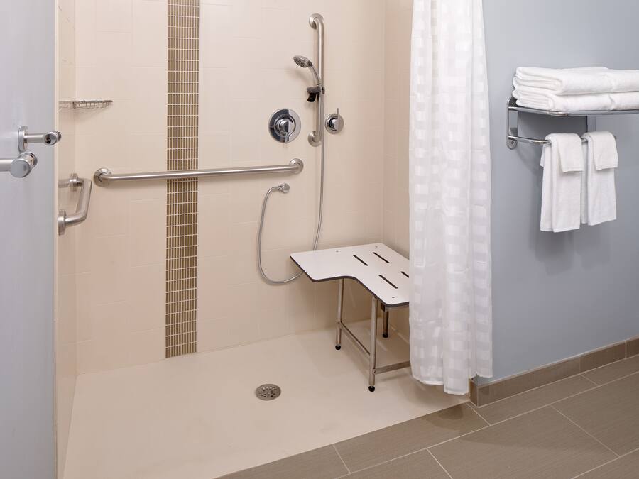 Un baño con ducha, barras de apoyo, toallero y asiento de ducha.