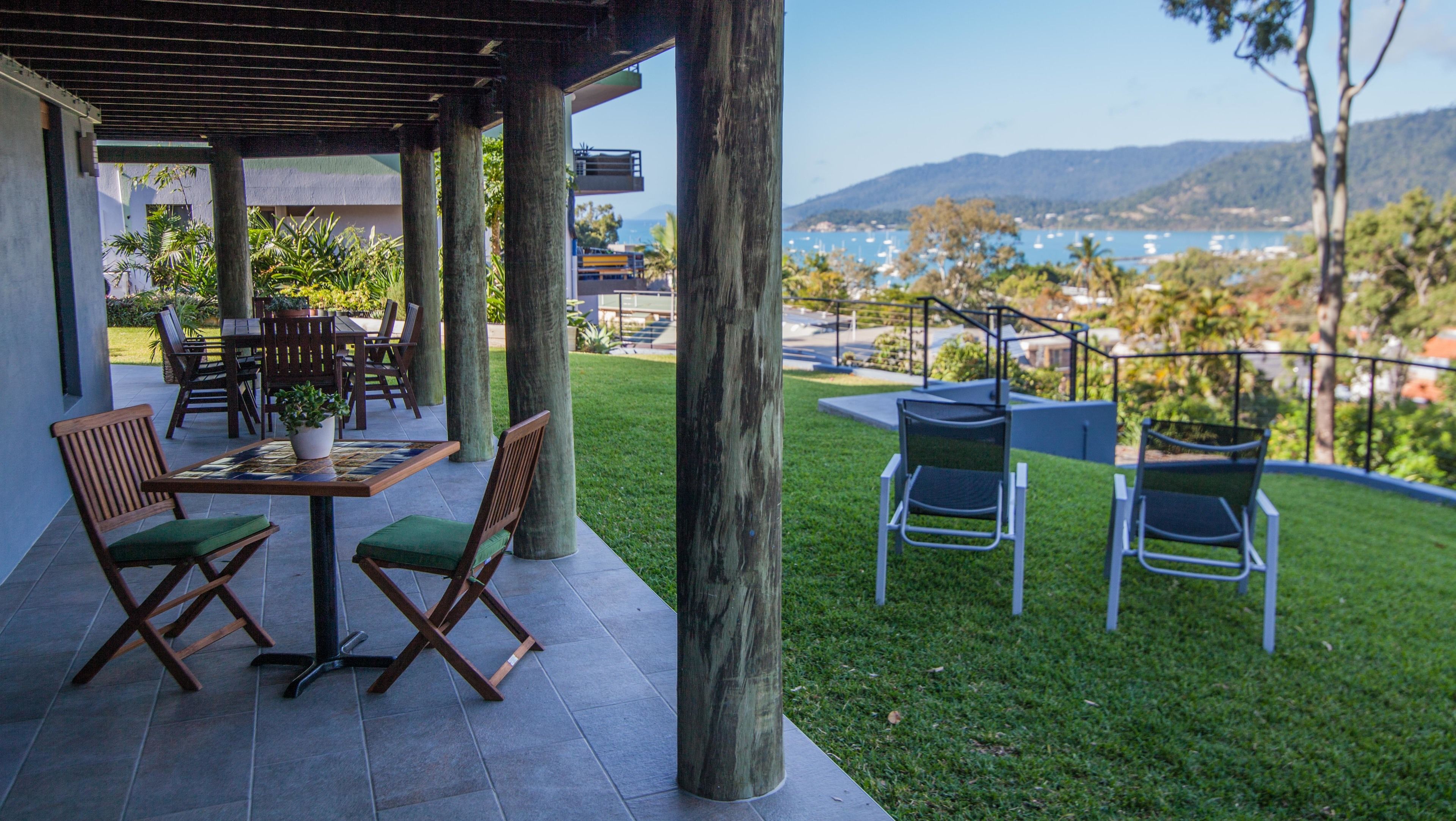 Une terrasse extérieure avec une table et des chaises, offrant une vue sur un plan d’eau et des collines en arrière-plan.