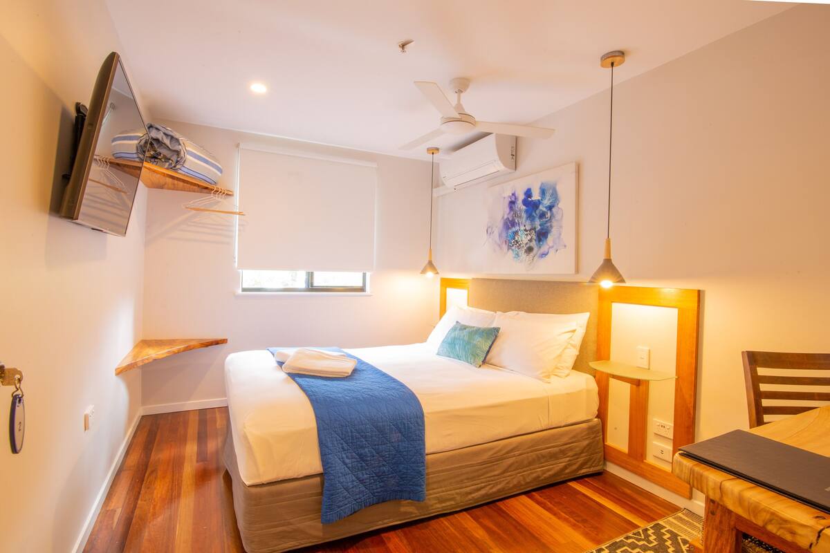 Un dormitorio con cama, mesita de noche, lámpara y ventilador de techo.