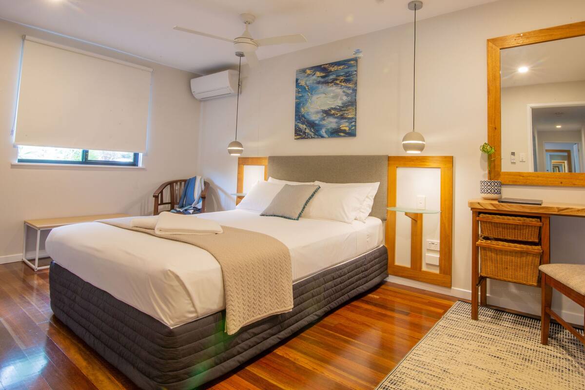 Un dormitorio con cama, mesitas de noche, una silla, un escritorio, un espejo y un cuadro en la pared.