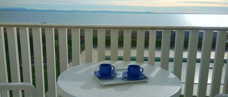 A balcony with a white table and two blue cups on a tray, overlooking a body of water and distant land.