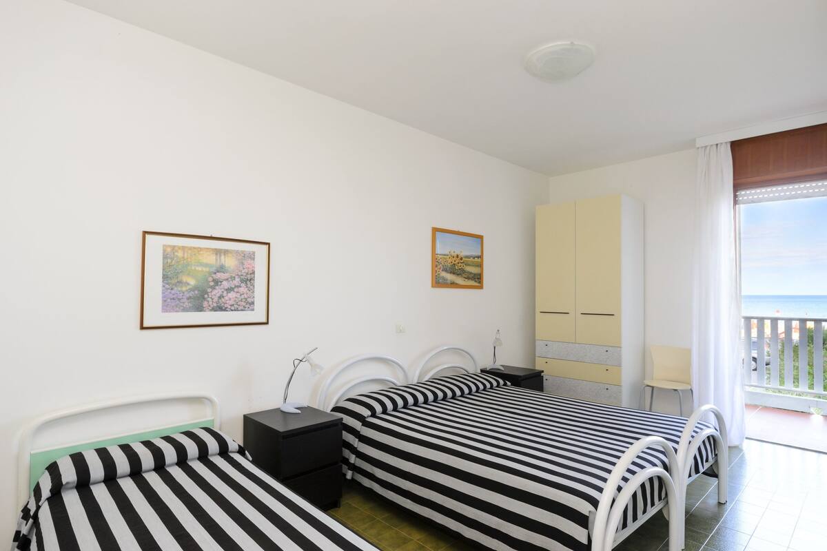A room with two beds, a small table, a chair, and a window with a view of the sea.