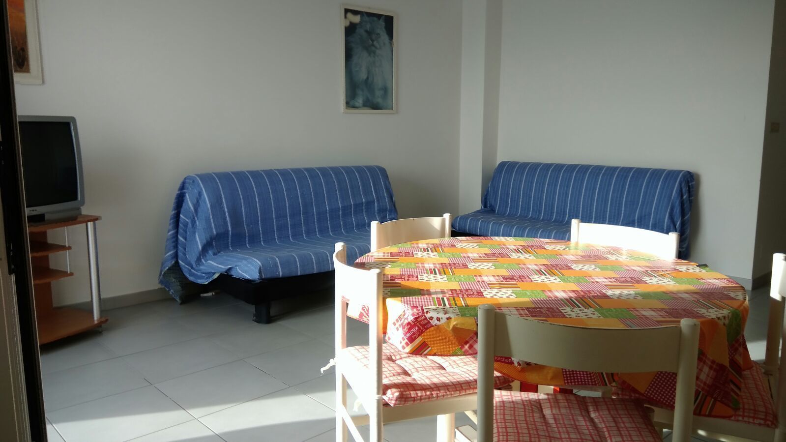 A room with a bed, a sofa, a dining table with chairs, and a television on a stand.