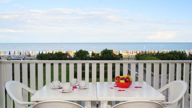 Een balkon met een tafel gedekt voor twee, met uitzicht op een strand met kleurrijke parasols en een helder zicht op de zee.