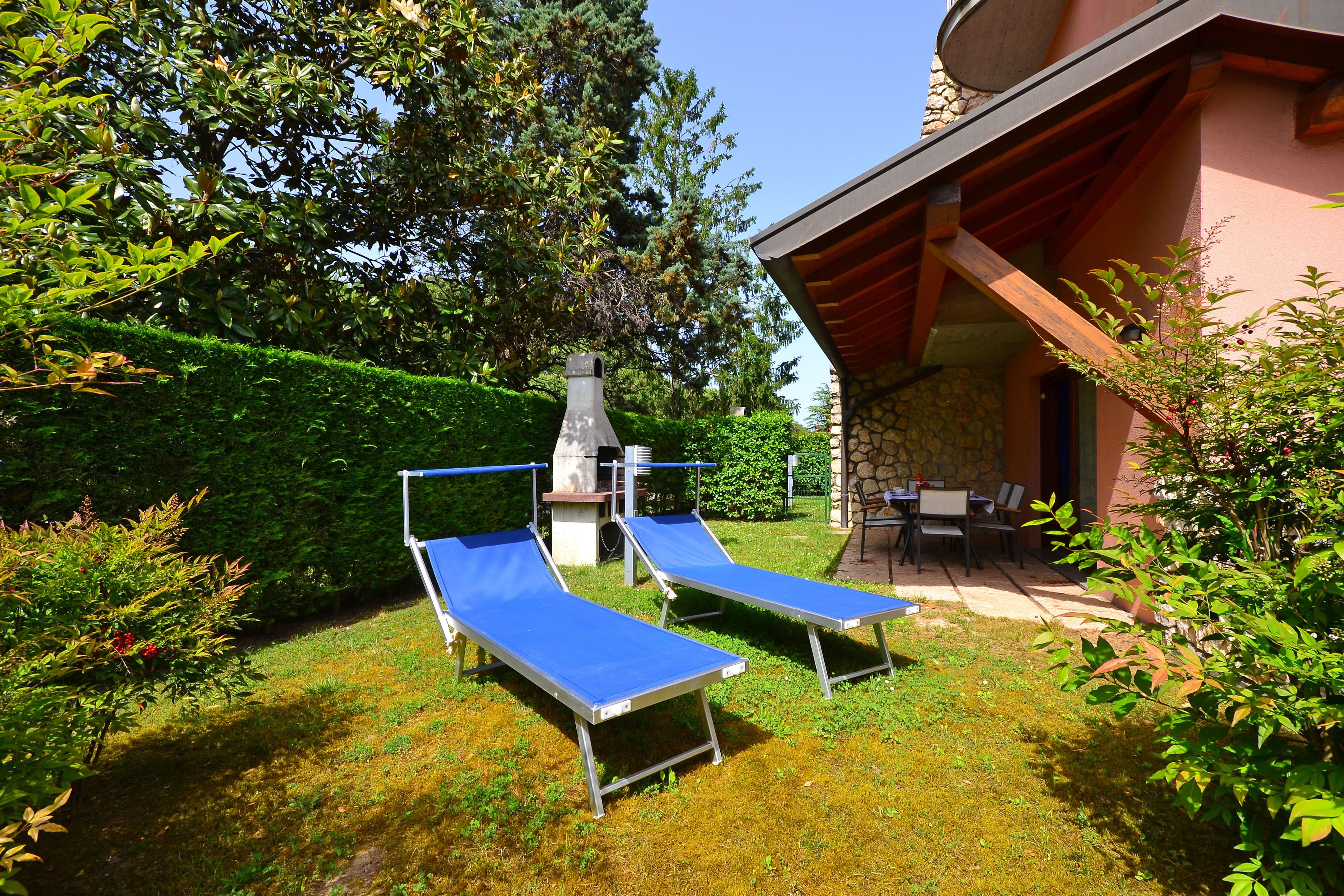 A patio area with two blue lounge chairs, a stone chimney, and a covered seating area with a table and chairs.