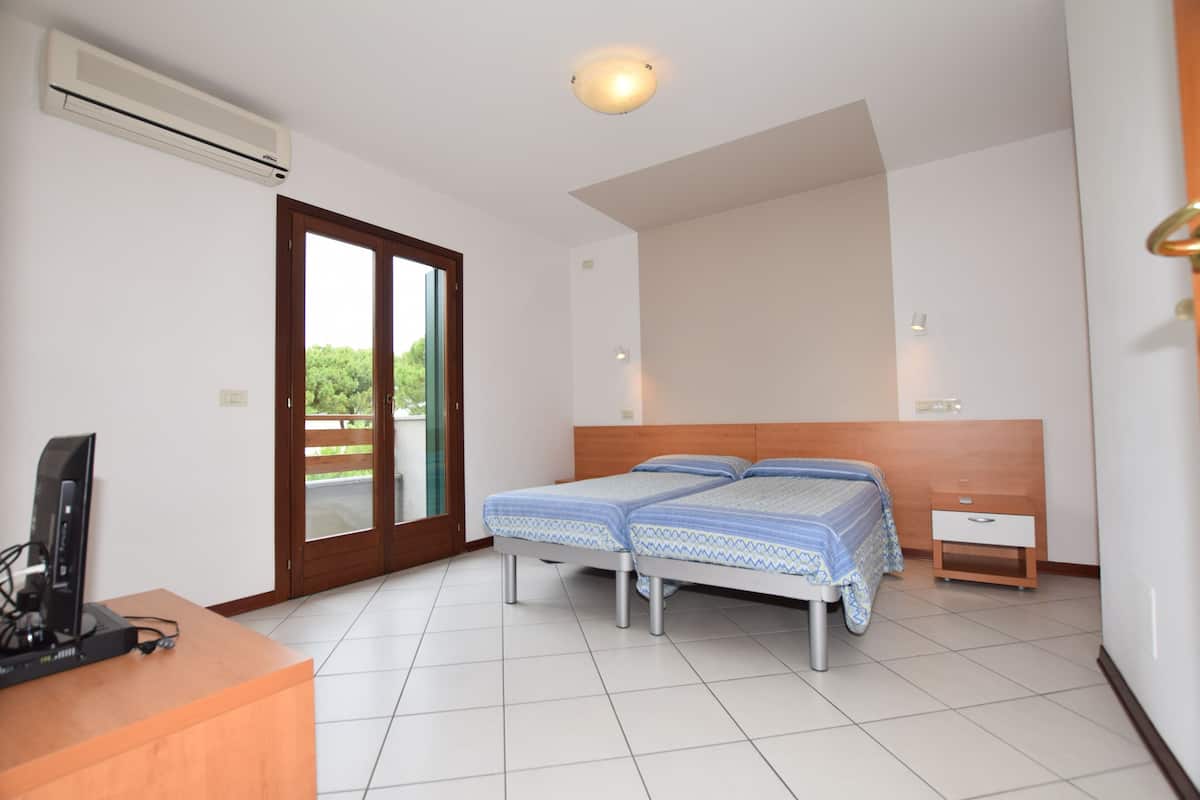 A hotel room with two beds, a desk with a computer, a nightstand, and a sliding glass door to the outside.