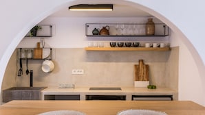 A modern kitchen with wooden countertops, a built-in sink, and a breakfast bar. There are shelves above the counter holding kitchenware and a potted plant. - 3 Caves Villa by Caldera Houses (Santorini)