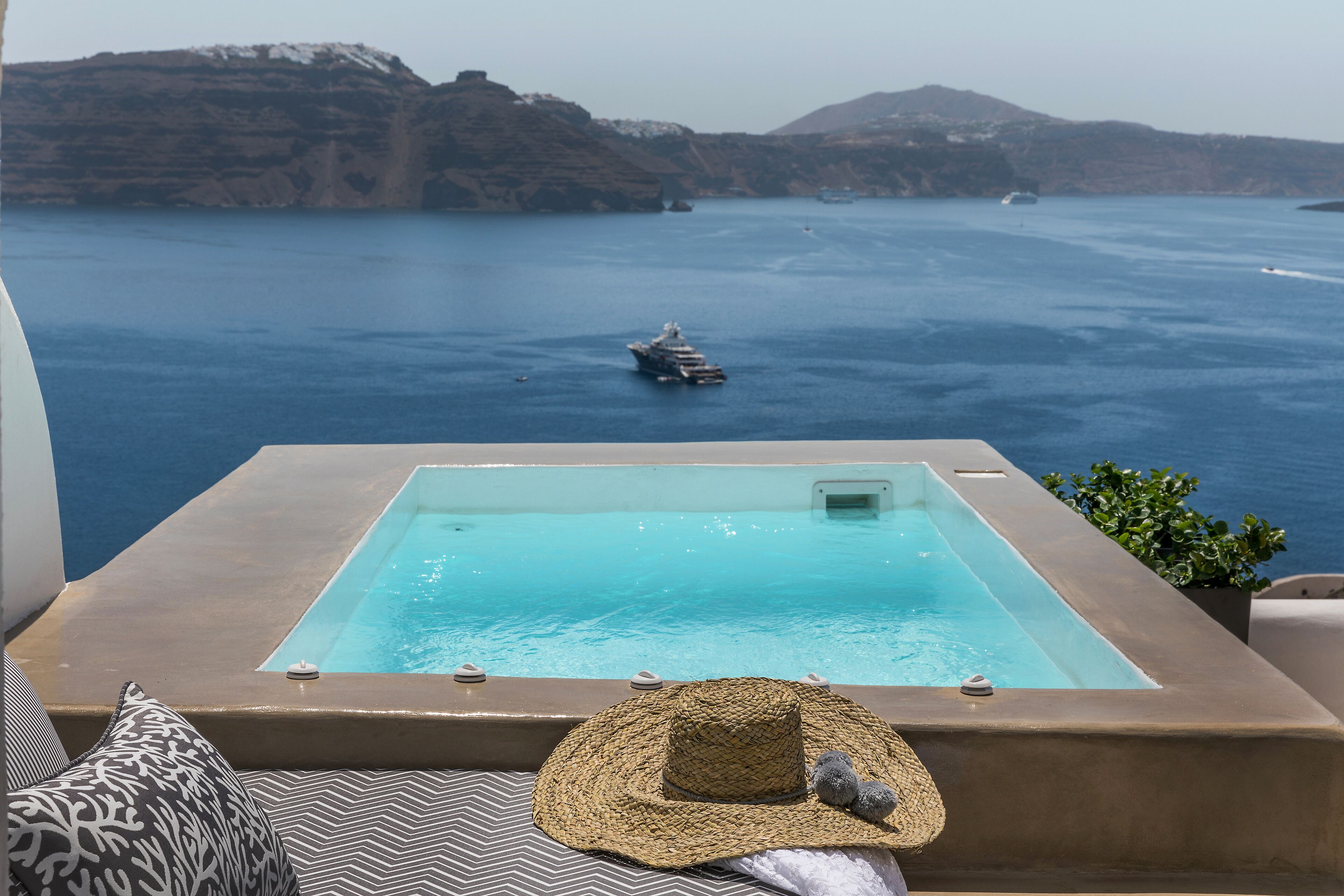 Zona de piscina con vista al mar, una silla de descanso, un sombrero y una pequeña planta.