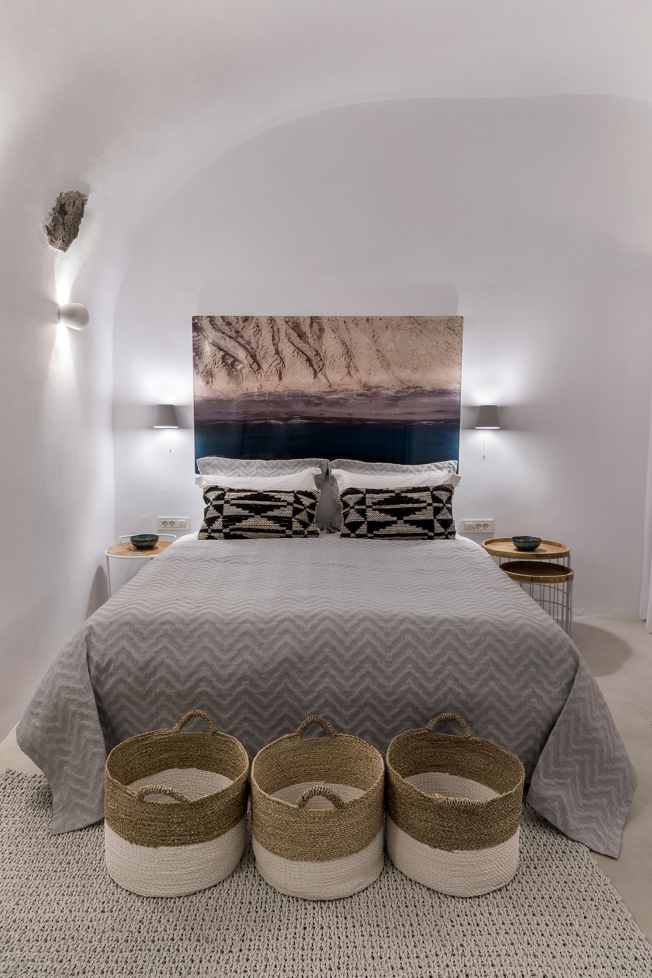 Un dormitorio moderno con una cama grande, un cuadro colgado en la pared, mesitas de noche y cestas decorativas.