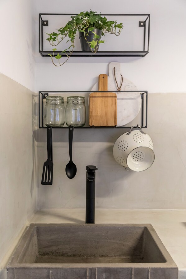 A kitchen with a built-in stove, two hanging shelves with jars, a colander, and a plant.