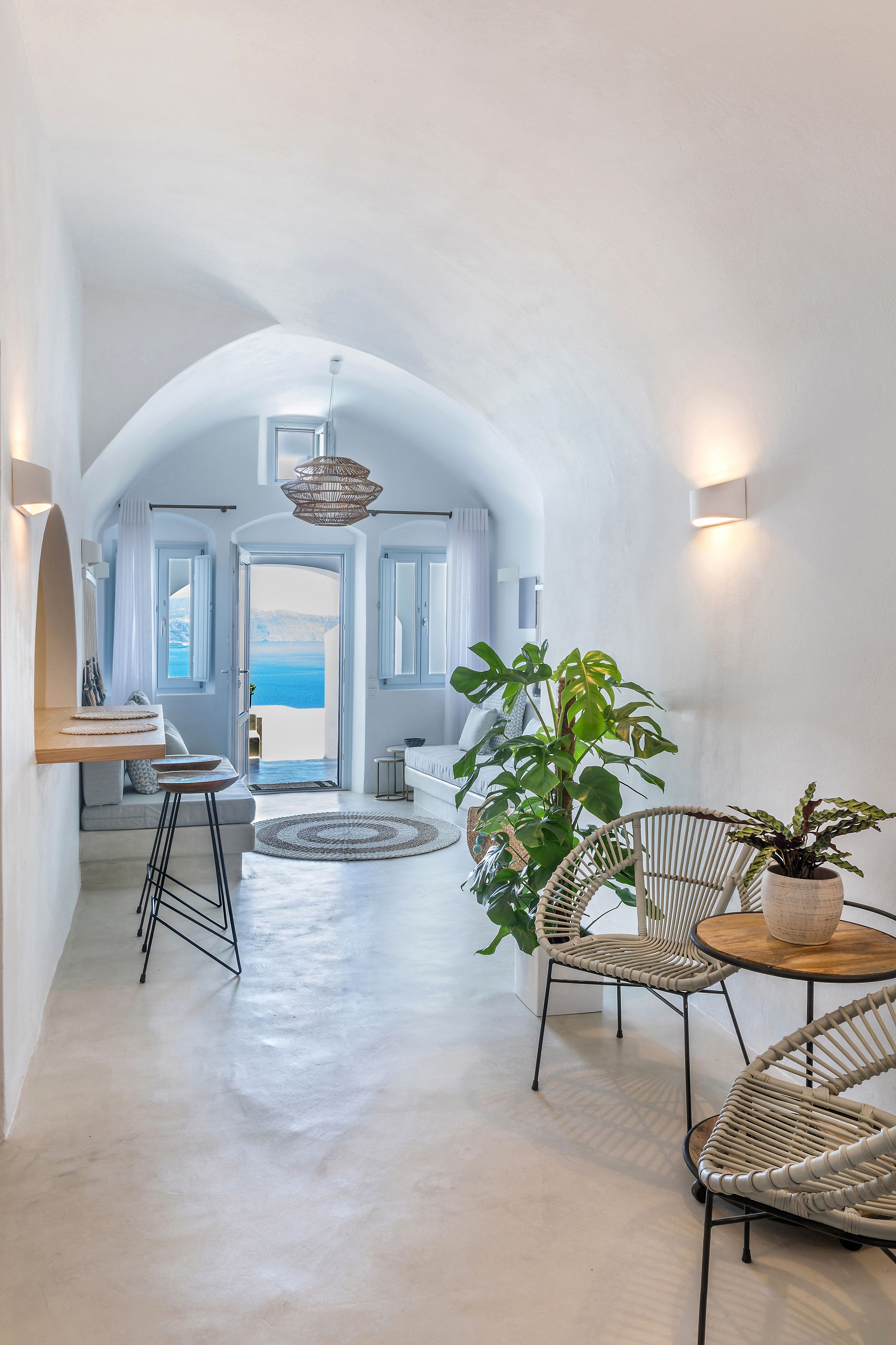 A modern interior with a view to the sea, featuring a round table, wicker chairs, and a large plant.