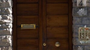 A wooden double door with a brass handle and a nameplate, set in a stone wall. - Nonna Lina Rooms (Florence)