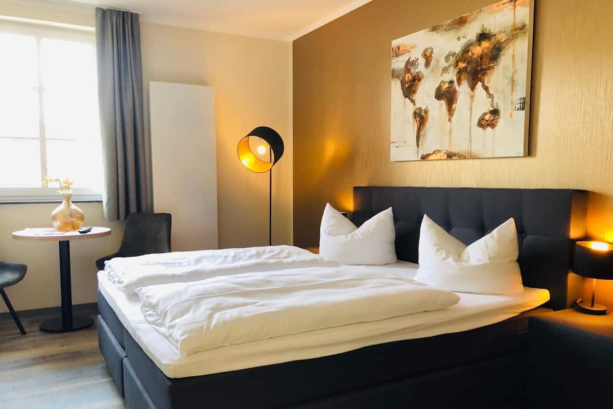A hotel room with a large bed, bedside tables, a desk, and a painting on the wall.