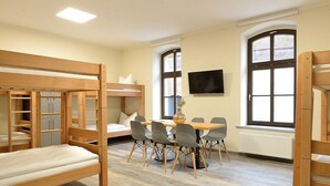 A room with bunk beds, a table with chairs, a flat-screen TV, and large windows. - Hostel & Pension  Alte Brauerei (Eisenach)