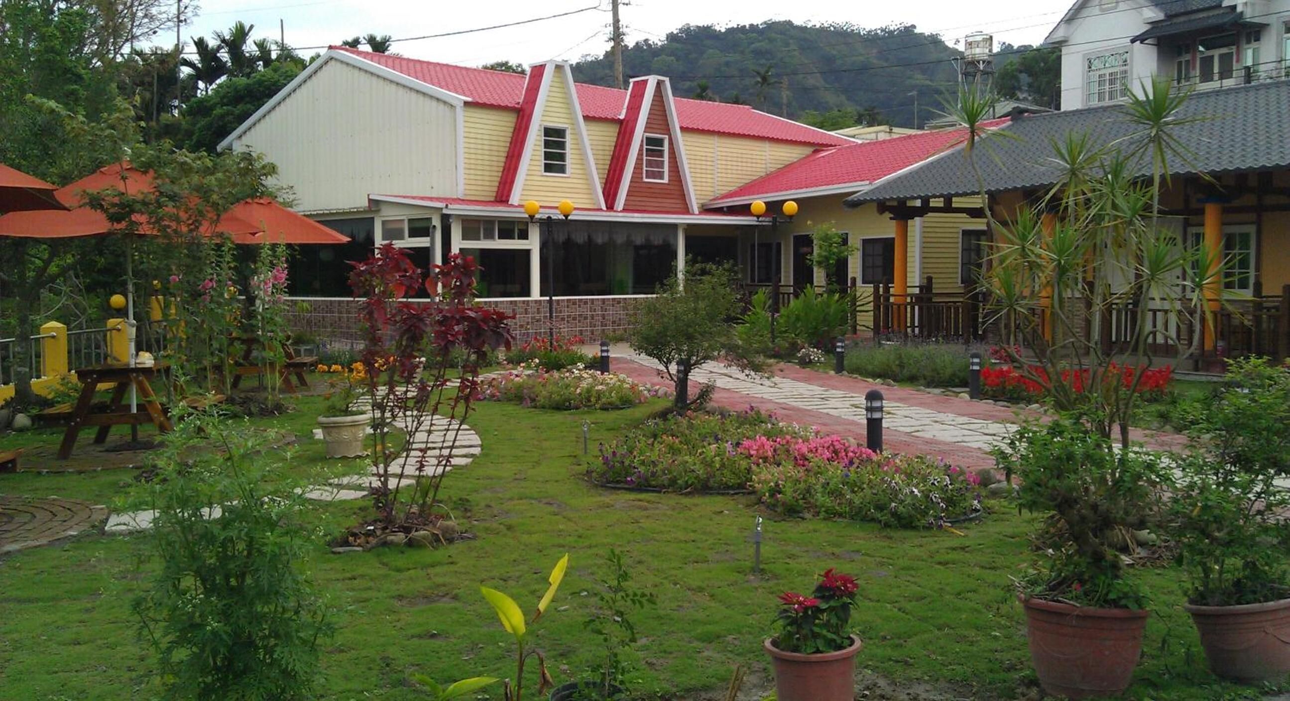A garden area with a patio, potted plants, and a building with a red roof.