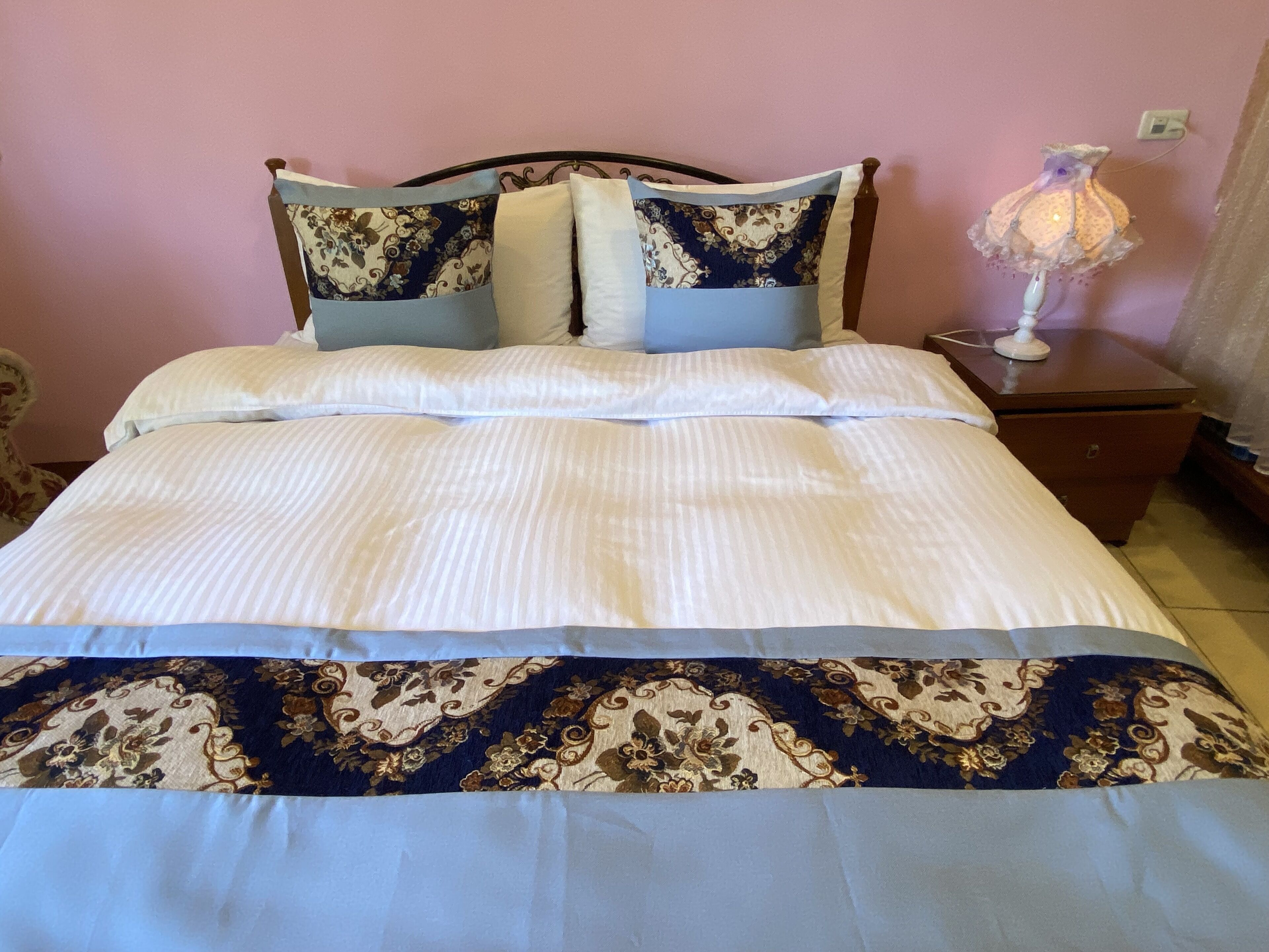 Ein Bett mit einer weiß-blauen Bettdecke, zwei passende Kissen und ein Nachttisch mit einer Lampe.