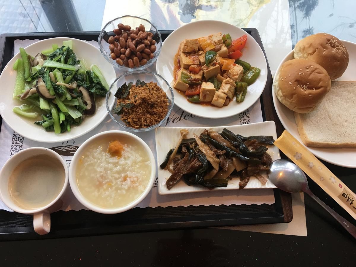 A tray with various dishes including tofu, vegetables, and soup, along with two cups and buns.