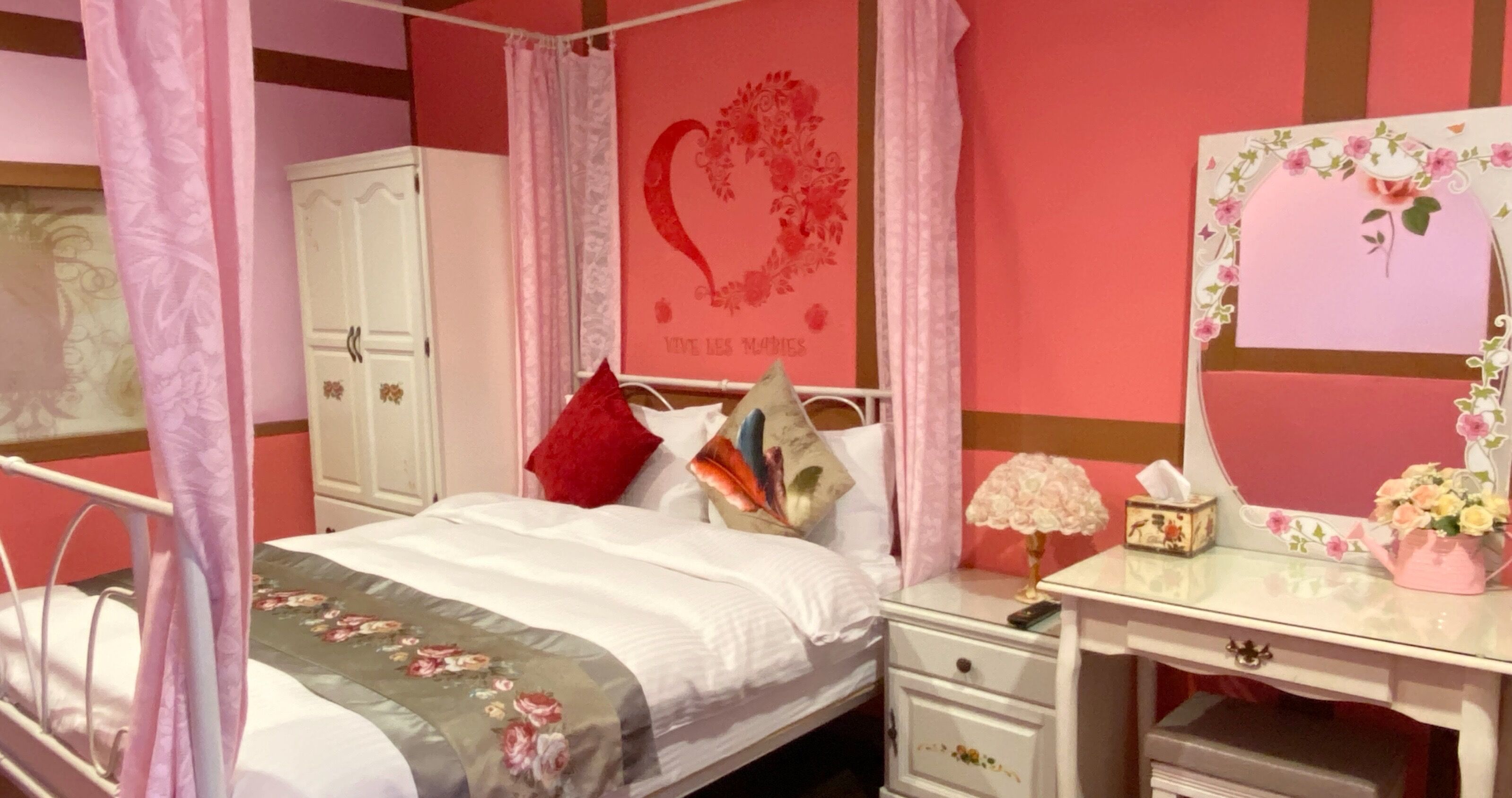 A bedroom with a bed, bedside table, dresser, and a wall with a floral design.