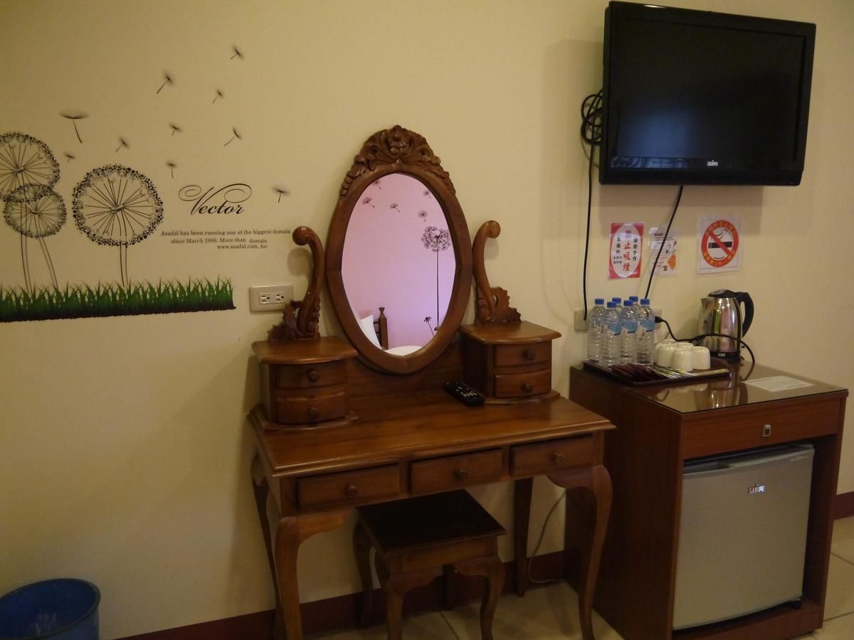 Un escritorio de madera con un espejo, un televisor montado en la pared y un refrigerador.