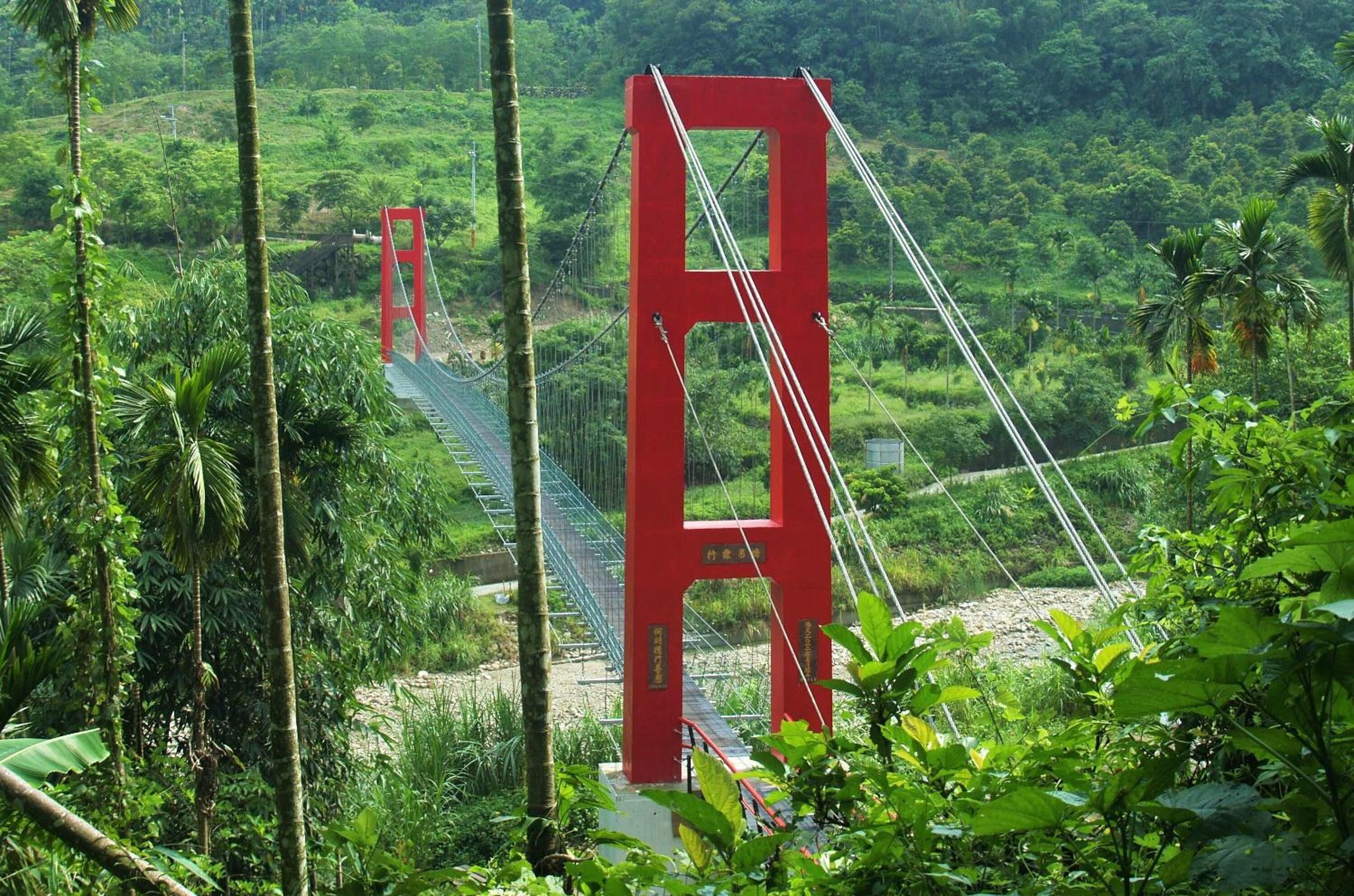Uma ponte suspensa vermelha em uma paisagem verde e exuberante.