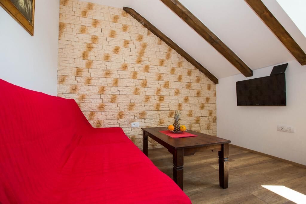 Een gezellige kamer met een rode bank, een houten tafel met fruit, een metselwerk muur en een wandtelevisie.